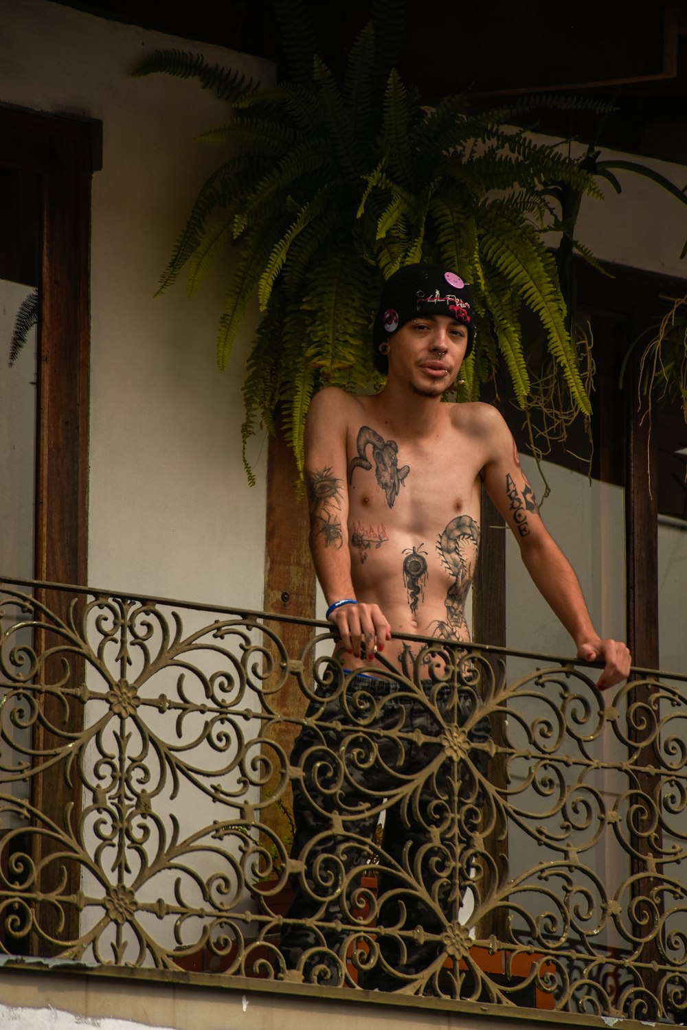 a shirtless man standing on a balcony next to a plant