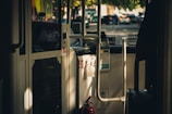 Interior view of a bus showing the driver's cabin and entrance area with a focus on the fare collection machine. Sunlight streams through windows, casting shadows on the interior surfaces. A fire extinguisher is visible near the door.