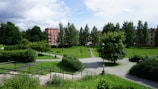 Green outdoor space with walking paths and benches near residential buildings.