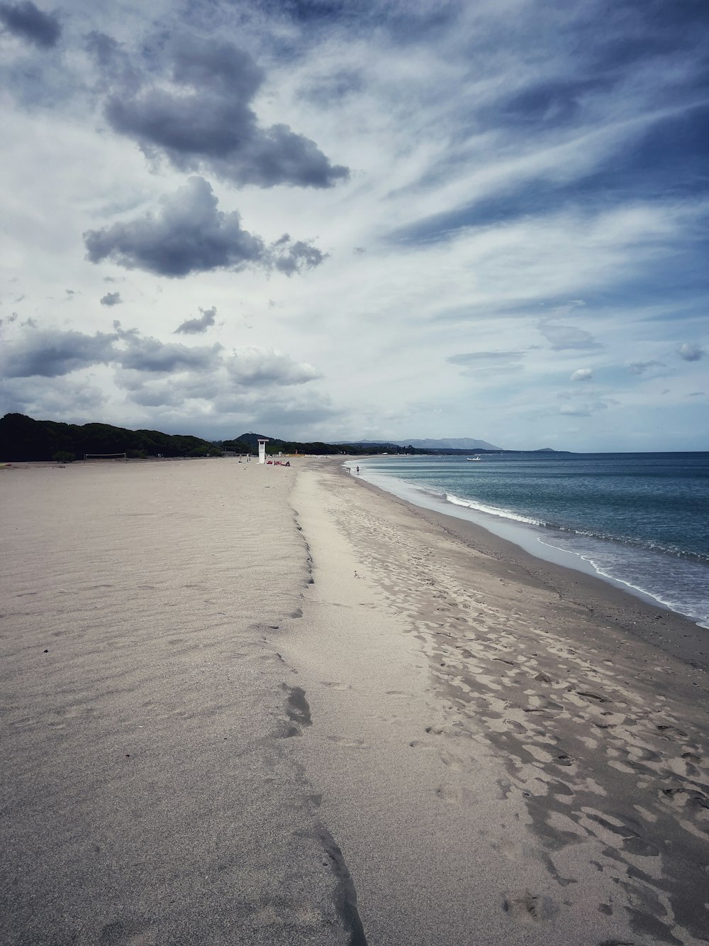 a sandy beach next to the ocean under a cloudy sky