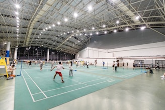 A vibrant badminton community gathering with players and fans interacting around courts and digital screens.