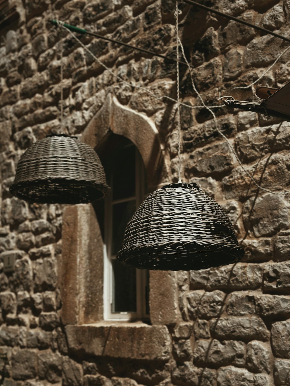 two wicker lamps hanging from the side of a stone building