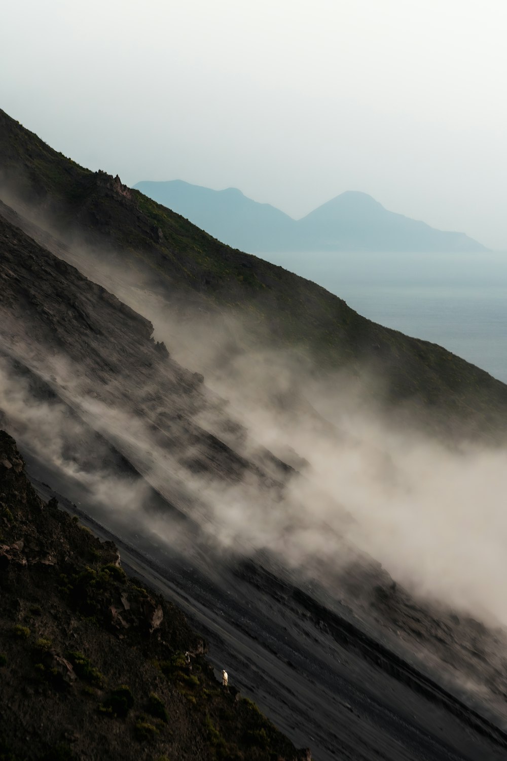 a hill covered in fog with mountains in the background