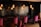 A stylish interior space featuring a set of plush magenta chairs and a comfortable couch along a wall tiled with dark, reflective bricks. Several pendant lights with warm, glowing bulbs hang from the ceiling, casting a cozy ambiance.
