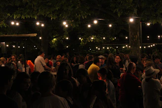 A lively neighborhood gathering with families chatting and kids playing under string lights.