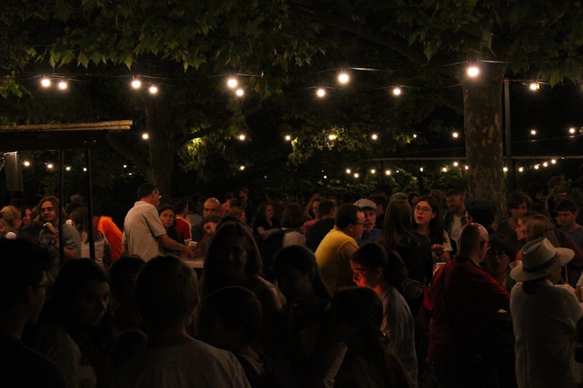 A lively crowd mingling at an outdoor event with string lights overhead in 2015.