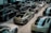 A showroom filled with multiple luxury cars parked in rows. The vehicles are sleek, modern, and exhibit a variety of models, predominantly in black, grey, and white finishes. The space is well-lit with reflections visible on the polished surfaces of the cars.