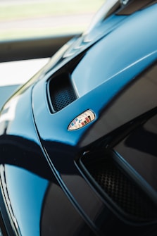 A close-up of a glossy car hood featuring a detailed emblem. The sleek design includes air vents that accentuate the vehicle's aerodynamic structure.