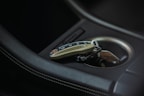 Elegant car key fob and sleek sunglasses placed on a black leather car seat with crimson stitching.