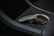 A luxurious car key fob rests in a car's cup holder, showing intricate design details and a logo. The setting includes sleek black leather with white stitching and a metallic interior accent.