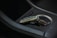 A luxurious car key fob rests in a car's cup holder, showing intricate design details and a logo. The setting includes sleek black leather with white stitching and a metallic interior accent.