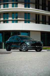 A sleek, black executive car parked in front of a modern building under soft golden lighting.