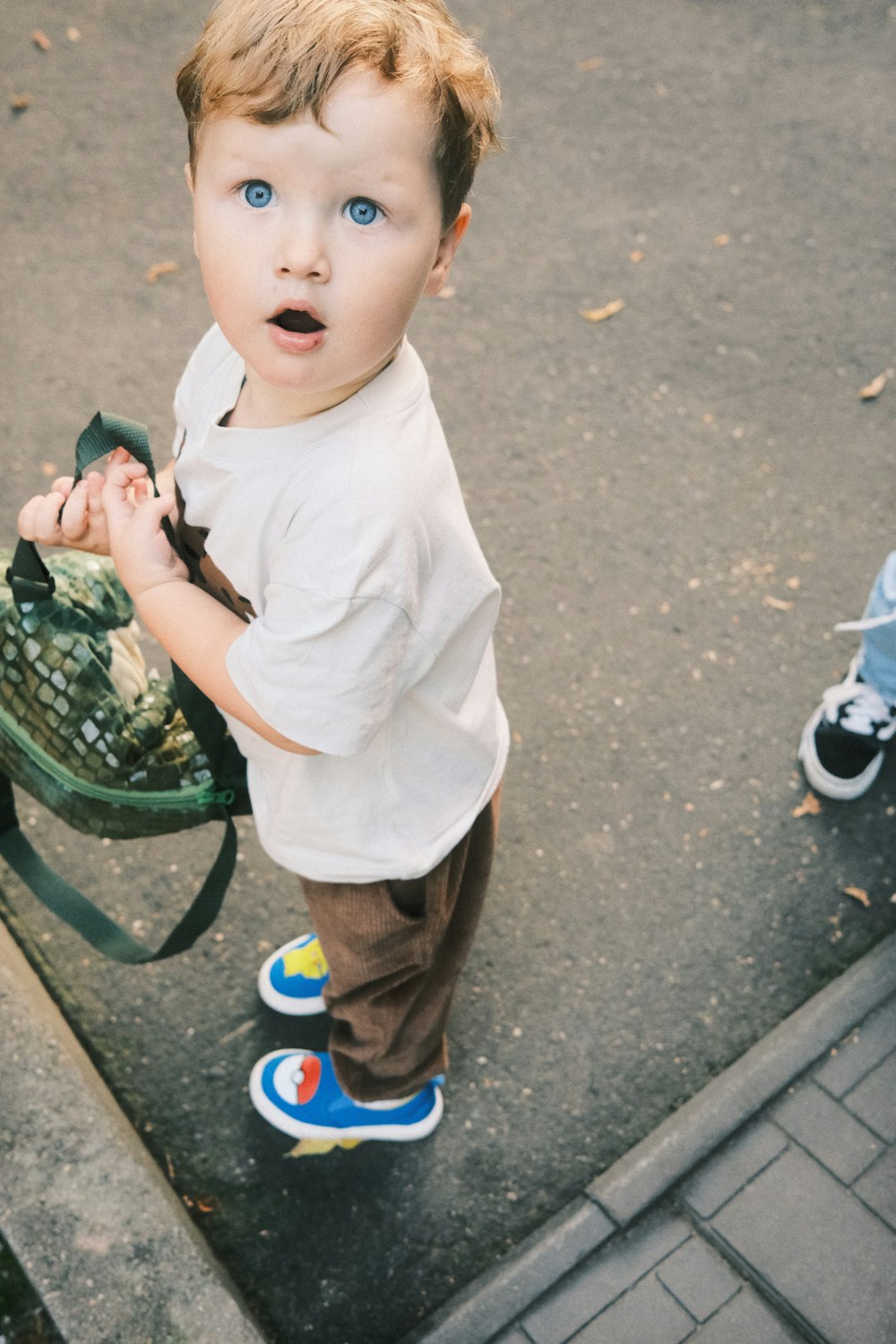 Un ragazzino in piedi su un marciapiede che tiene uno zaino