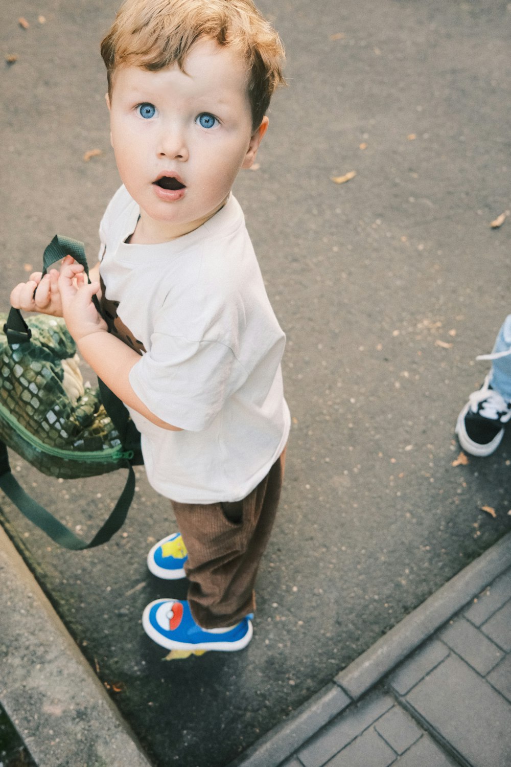 a little boy standing on a sidewalk holding a backpack