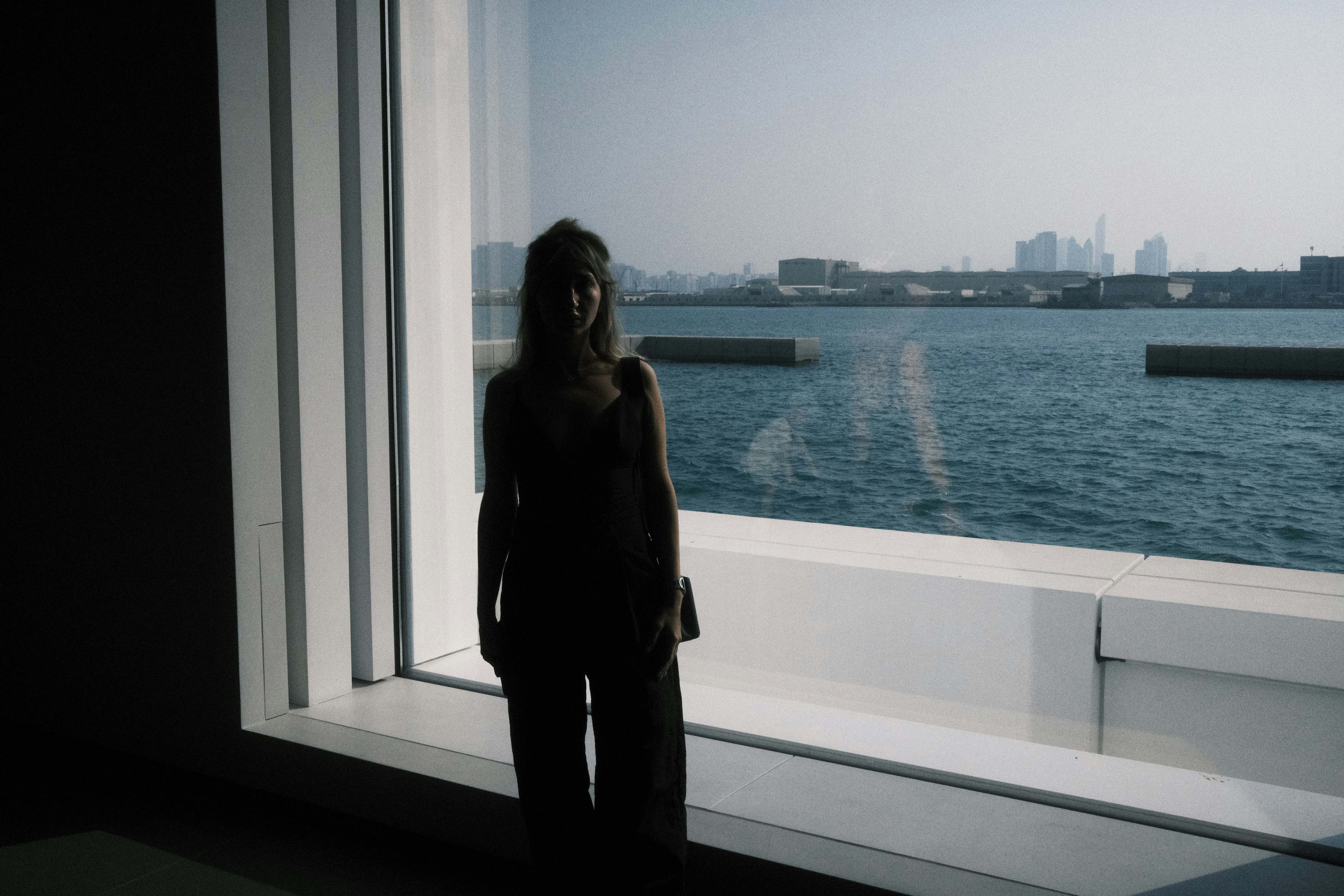a woman standing in front of a window next to a body of water
