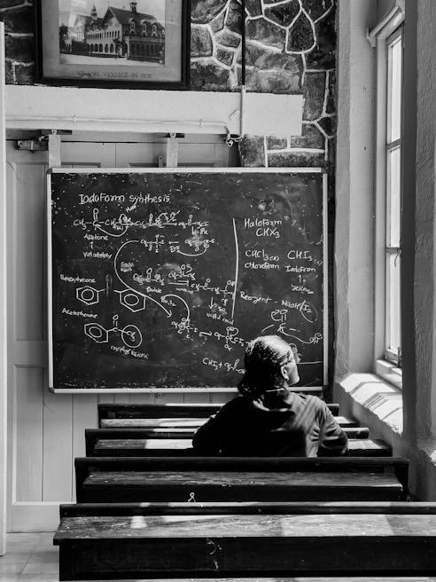 A modern classroom featuring a digital board displaying a chemistry diagram, with students engaged in discussion.
