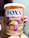 A hand holds a colorful tin of FOX's Crystal Clear Fruits which features vibrant imagery of fruits and multicolored candy. The tin is labeled with lemon, strawberry, blackcurrant, and orange flavors. The packaging includes bold blue and orange colors with images of fruit slices and candies.