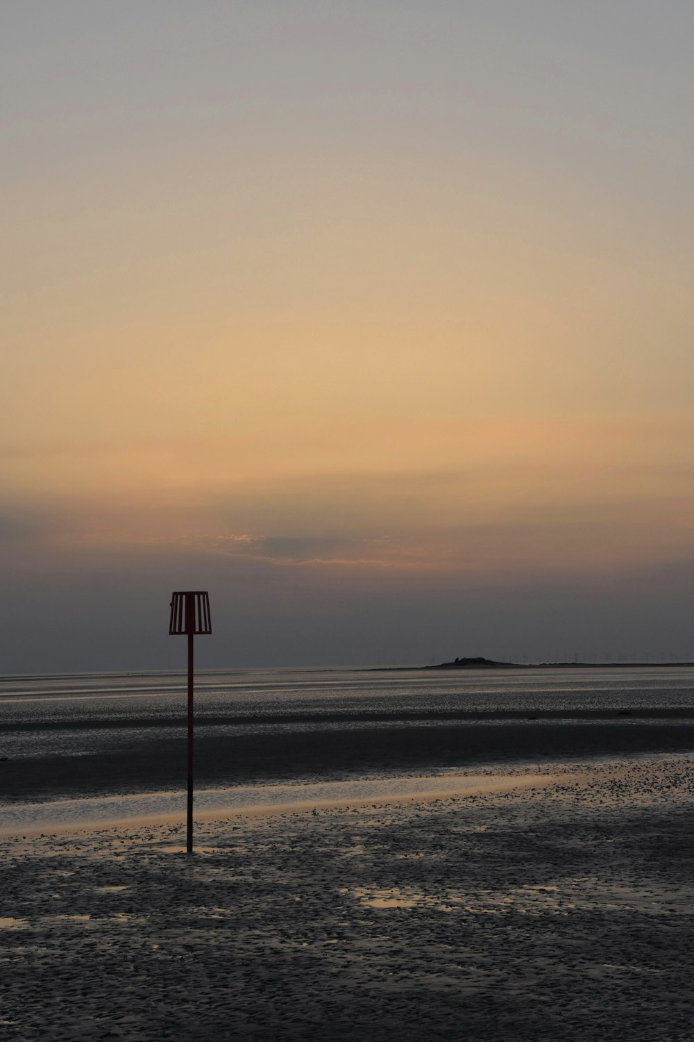 a pole in the middle of a beach at sunset