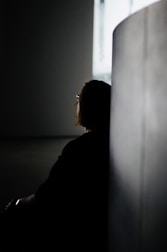 a woman sitting in a dark room next to a wall