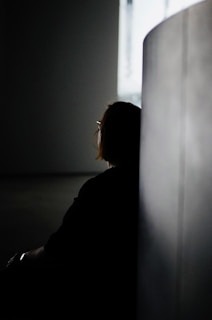a woman sitting in a dark room next to a wall