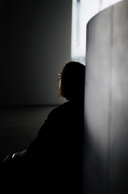 a woman sitting in a dark room next to a wall