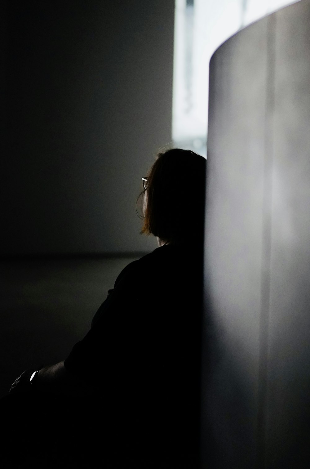 a woman sitting in a dark room next to a wall