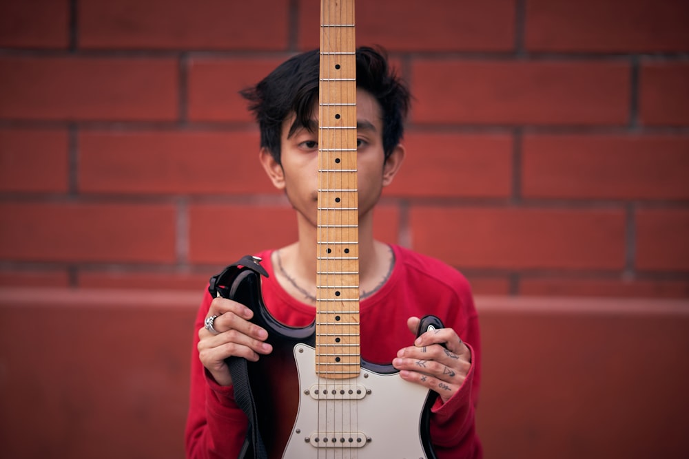 a person holding a guitar in front of a brick wall