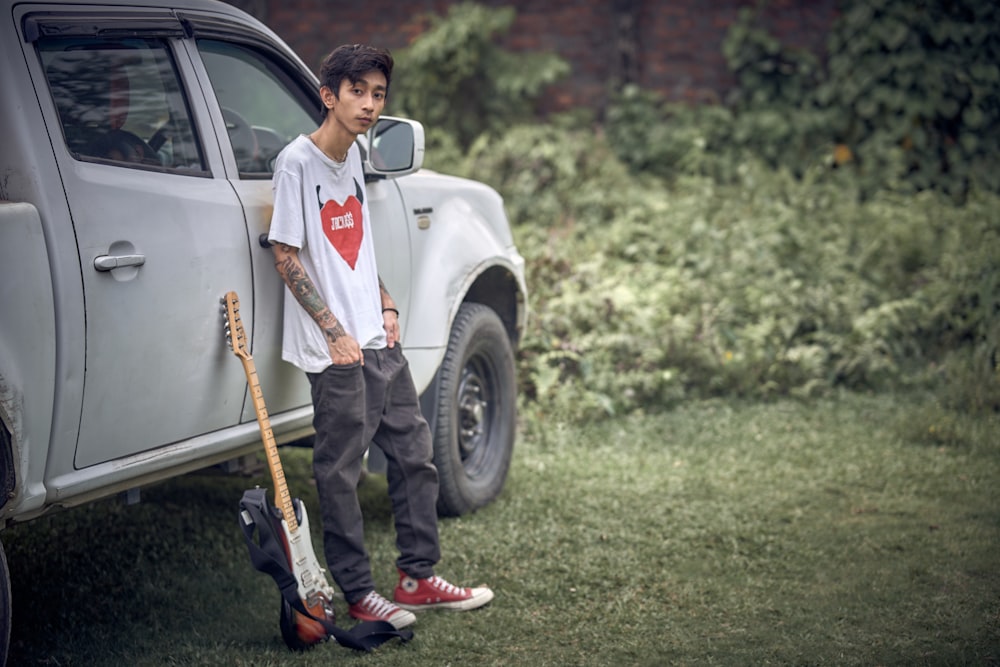 a young man standing next to a truck holding a guitar