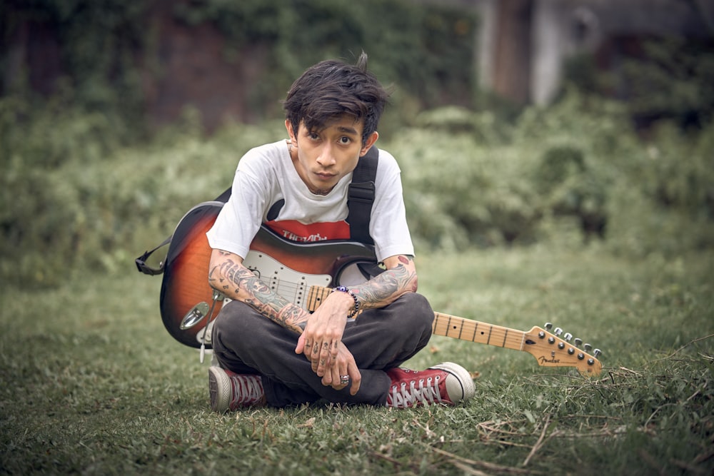 a young man sitting on the ground with a guitar