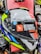 A close-up view of a motorcycle helmet is displayed prominently against a red background. The helmet features a mixture of bright and reflective colors, including neon yellow, blue, white, black, and silver. There is a large sticker on the visor with text reading 'Designed to Protect' and a website URL 'www.mthelmets.com'. A blue sticker indicating quality control pass (QC PASSED) is also affixed near the visor mechanism. The environment shows other helmets and equipment, indicating a store setting.