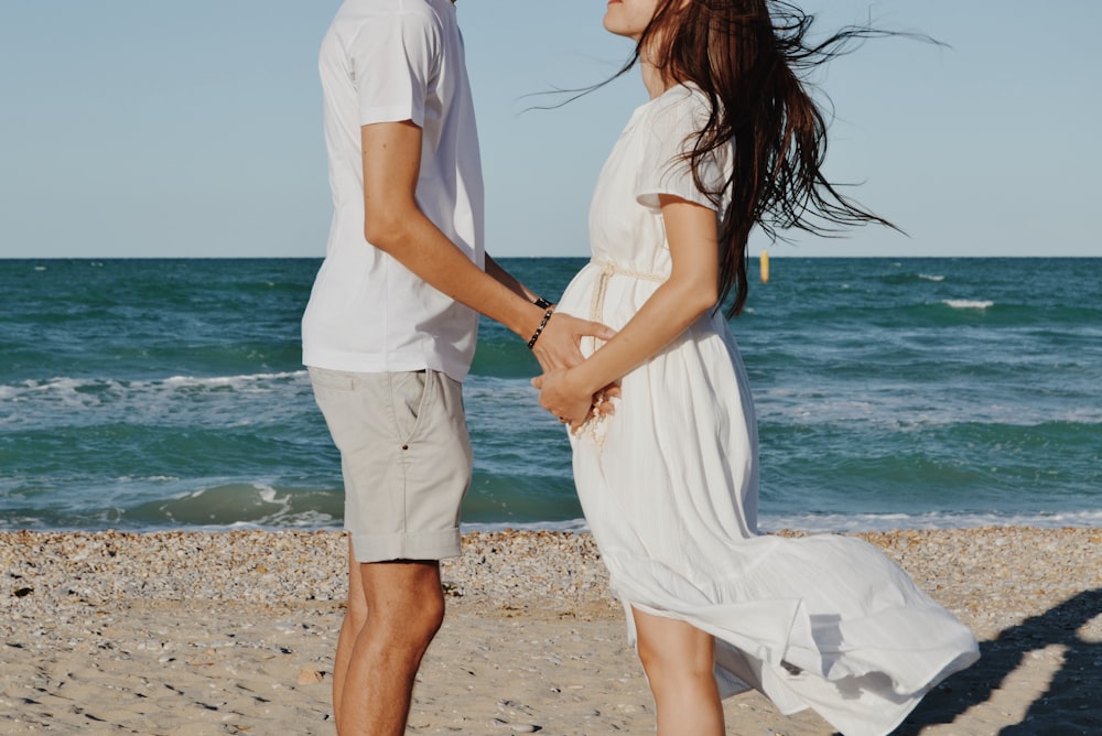 a man and a woman standing on a beach next to the ocean