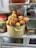 A refrigerator shelf with a pot filled with fresh peaches. The pot is surrounded by other containers and jars inside the refrigerator.