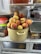 A refrigerator shelf with a pot filled with fresh peaches. The pot is surrounded by other containers and jars inside the refrigerator.