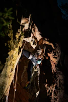 A climber wearing a harness and helmet scaling a steep cliff at sunset