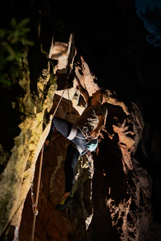A climber wearing a harness and helmet scaling a steep cliff at sunset