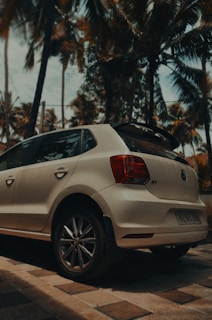 A bright Toyota Agya parked by a palm tree with turquoise ocean in the background
