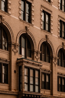 An architectural close-up of a historic building facade featuring ornate details such as decorative moldings, brickwork, and arched windows. The design showcases a traditional style typical of older urban construction.