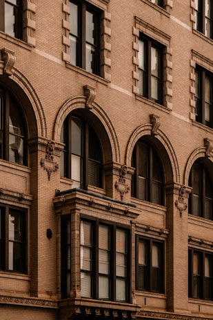 An architectural close-up of a historic building facade featuring ornate details such as decorative moldings, brickwork, and arched windows. The design showcases a traditional style typical of older urban construction.