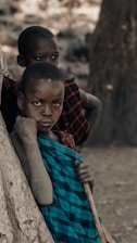 two young boys standing next to each other near a tree