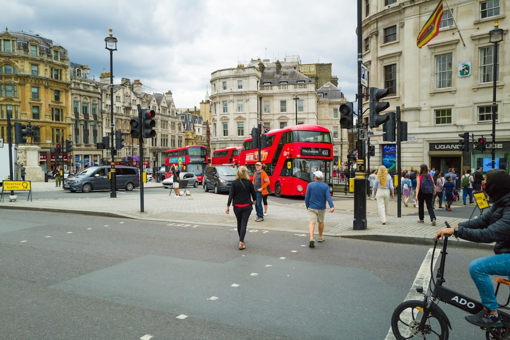 a group of people walking across a street next to a red double decker bus