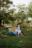 A happy customer lounging on a wicker bench in a garden during light rain.