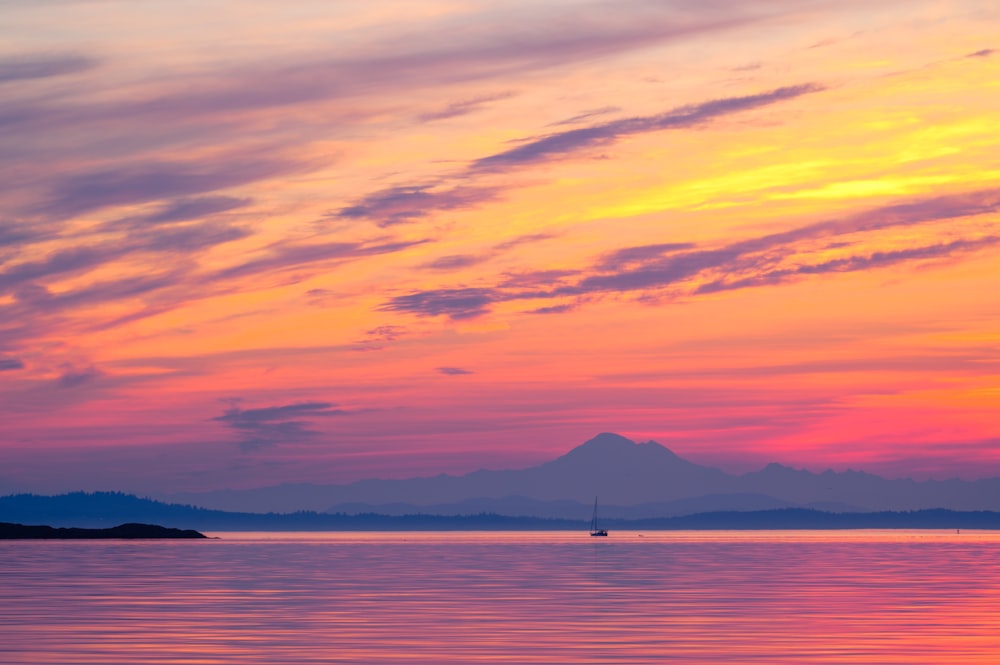 a boat in the water at sunset with a mountain in the background