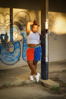 A model wearing a deep navy polo shirt leaning against a graffiti-covered brick wall at sunset.