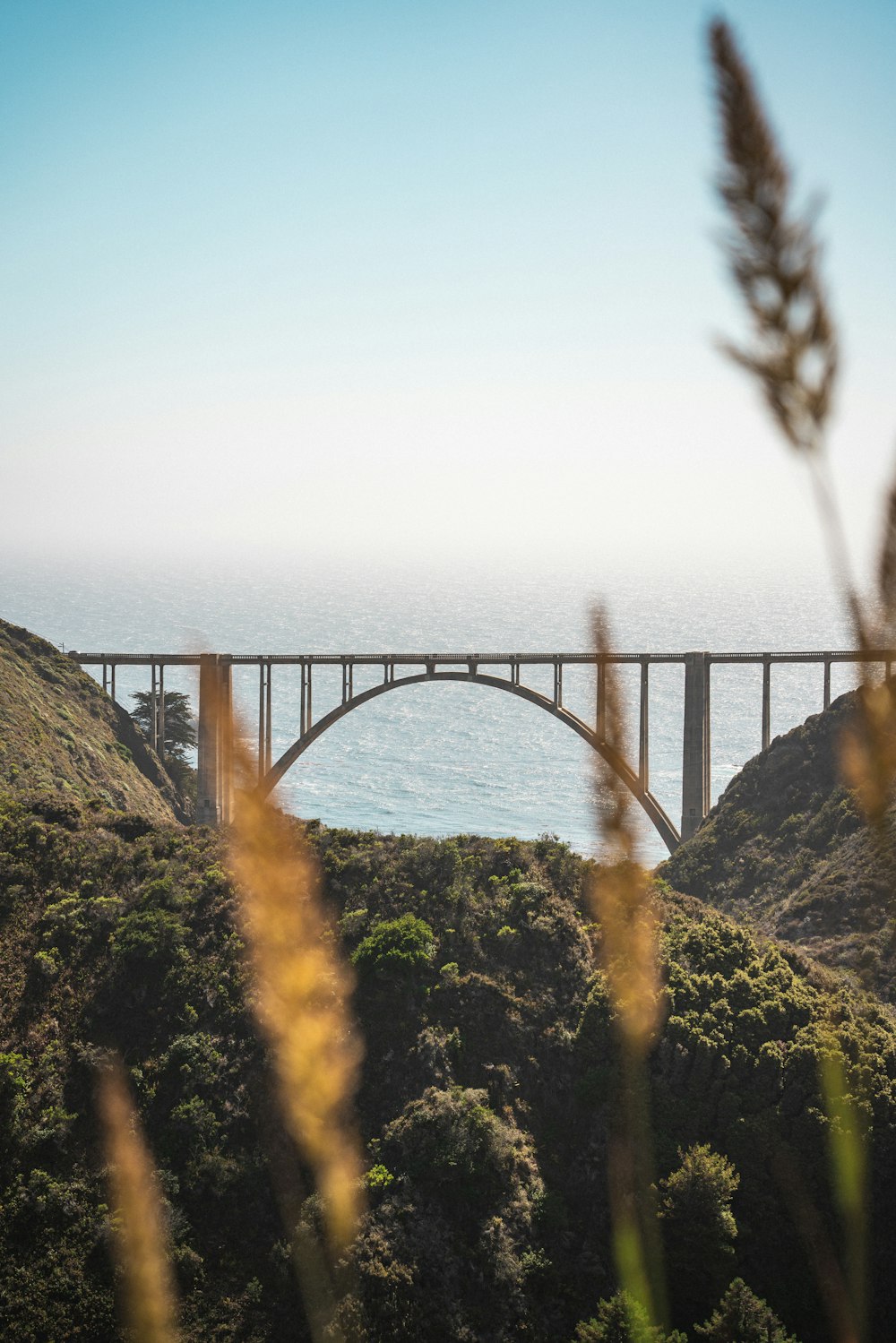 a bridge over a body of water next to a lush green hillside