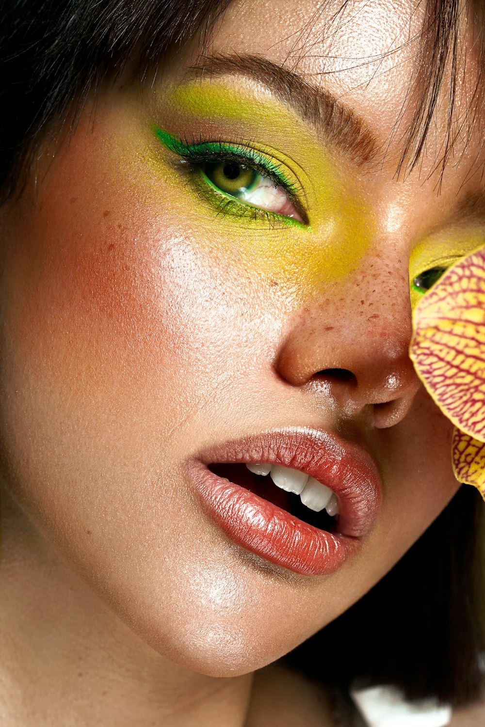 a woman with green and yellow makeup holding a flower