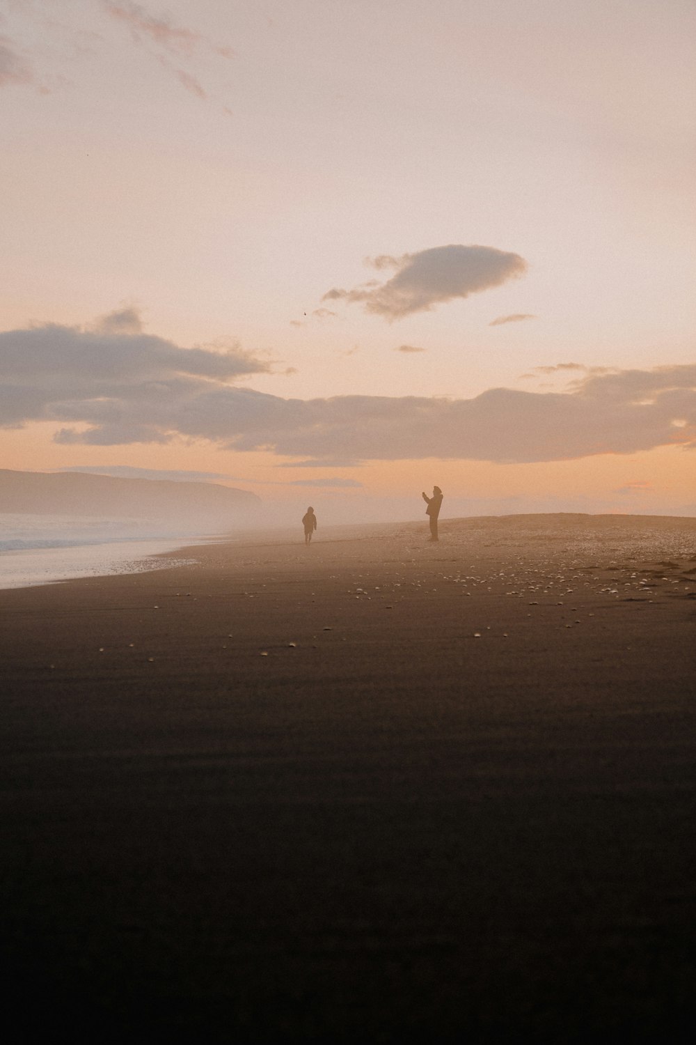 a couple of people standing on top of a sandy beach