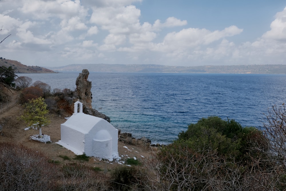 a small white building sitting on top of a hill next to the ocean