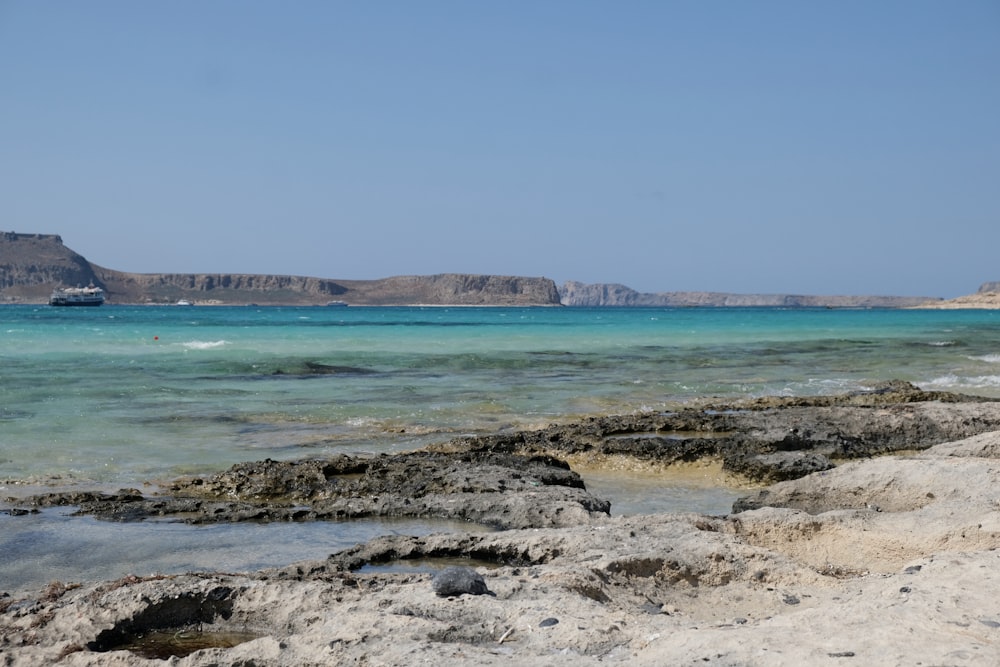 a rocky beach with clear blue water and mountains in the background