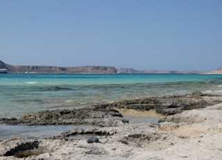 a rocky beach with clear blue water and mountains in the background