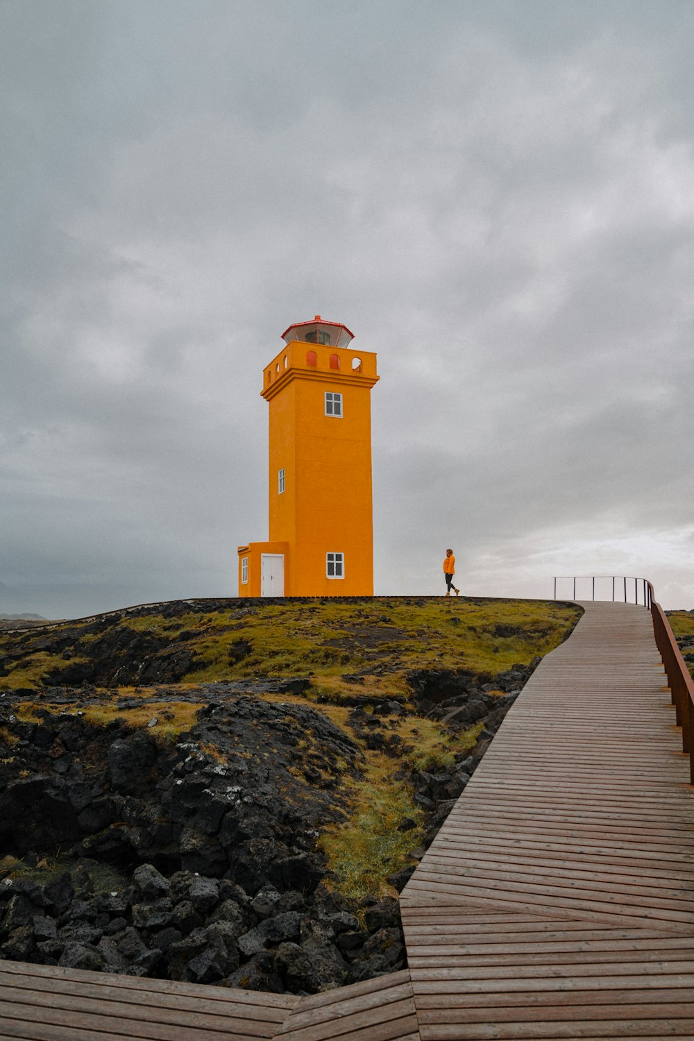 Ein Holzsteg, der zu einem gelben Leuchtturm führt